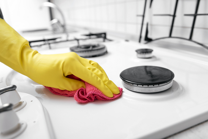 yellow rubber gloves and bright pink cleaning cloth cleaning white stove top